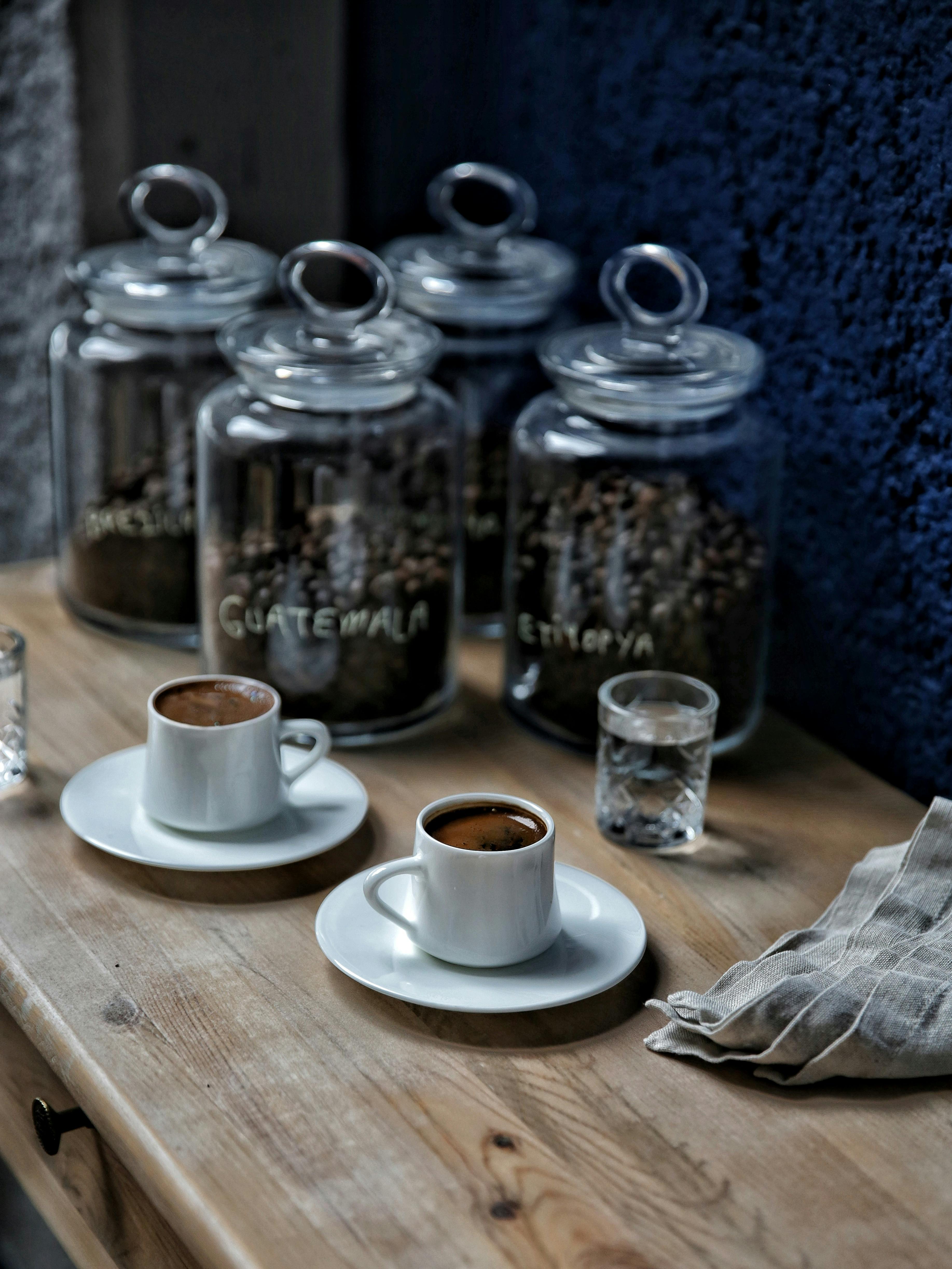 Espresso cups with water glasses on a wooden table, surrounded by coffee jars from Guatemala and Ethiopia.