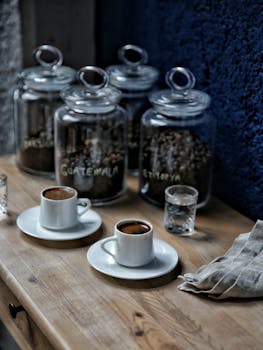 Espresso cups with water glasses on a wooden table, surrounded by coffee jars from Guatemala and Ethiopia.