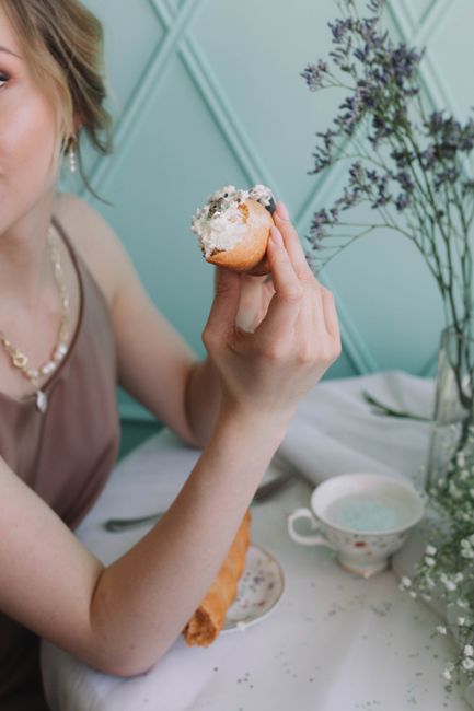 Woman enjoying a pastry at a café table with a delicate flower arrangement.