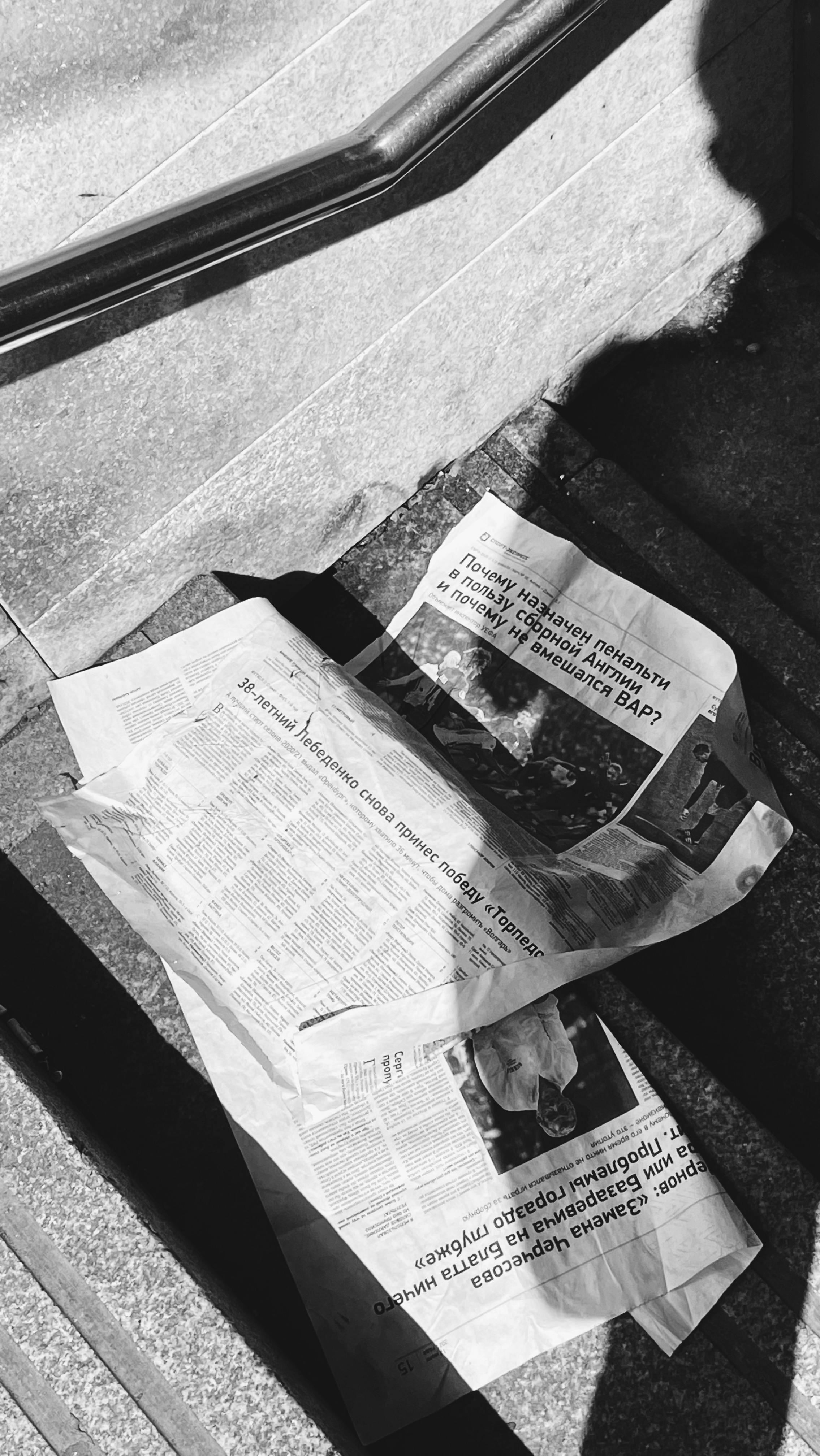 Black and white newspapers on stairs with shadow play, creating a dramatic effect.