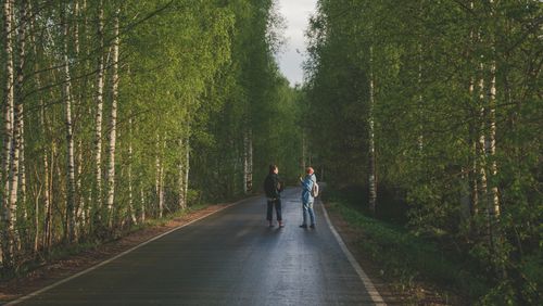 Free Two individuals strolling along a tree-lined road, surrounded by lush green forest. Stock Photo