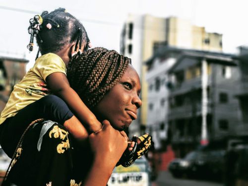 Free A heartwarming moment of a mother carrying her daughter on her shoulders, set in Lagos, Nigeria. Stock Photo