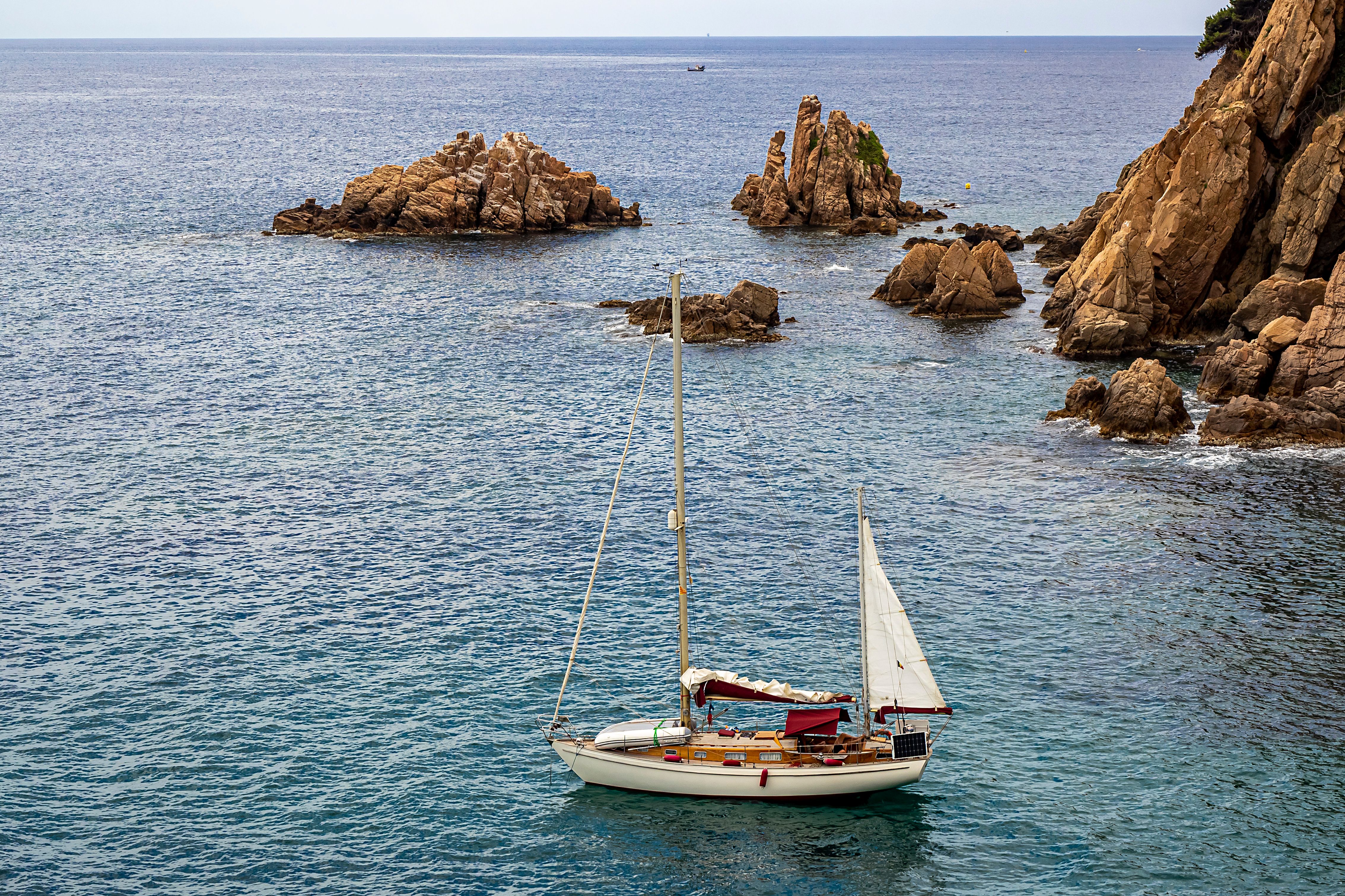 Amazing Barcelona Unique Private Luxury Sailing Tour (max 12 people) Review: A Luxurious Mediterranean Escape Worth Every Euro Review 2026 - A sailboat glides through the rocky coastline of Blanes, Spain's picturesque seascape.