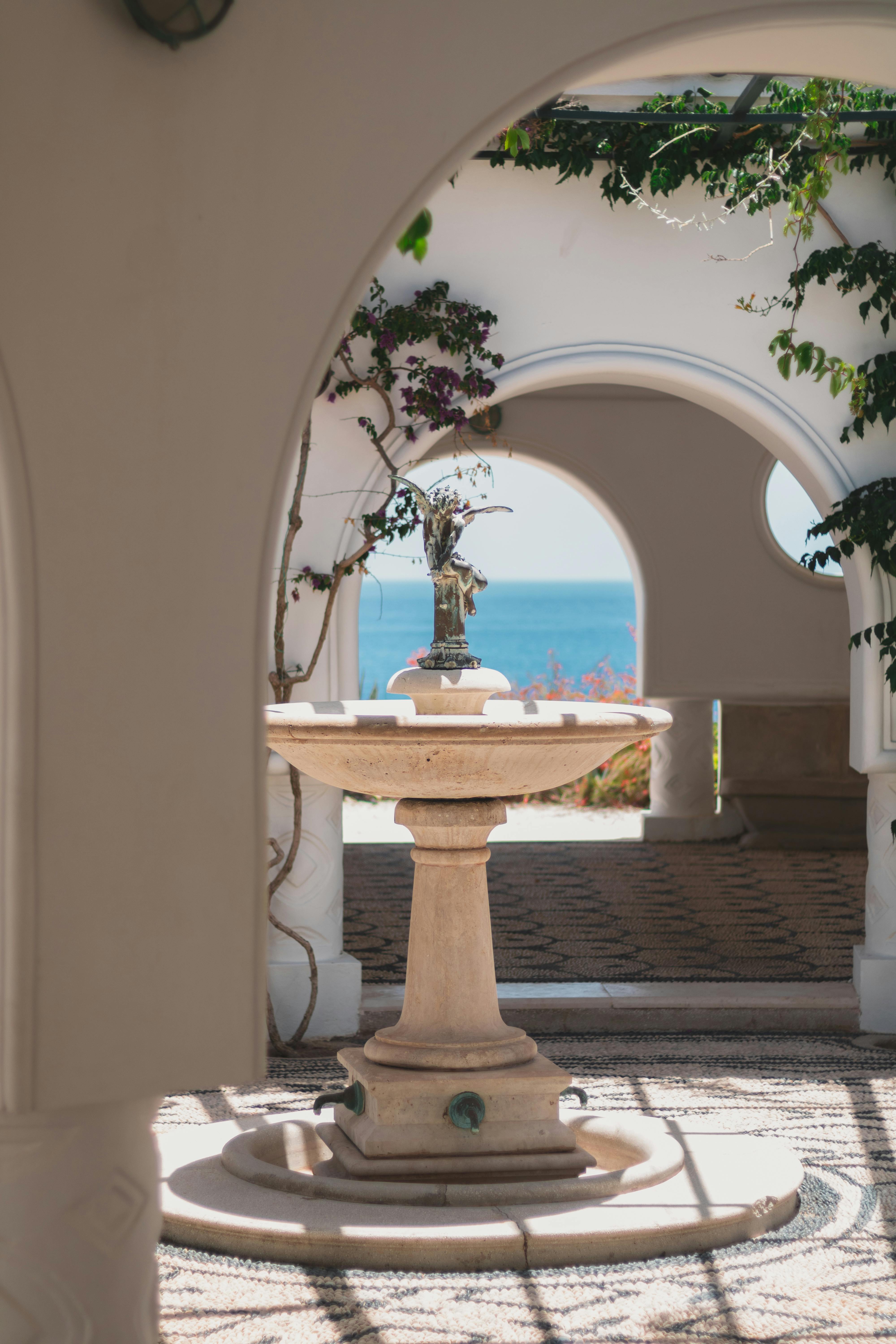 A picturesque fountain framed by arched architecture, overlooking a serene sea view.