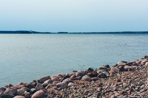 Free Tranquil scene of a pebble-strewn shore against a vast lake under a clear sky. Stock Photo