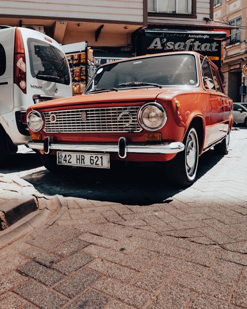 Free A classic red Lada 2101 parked on a sunlit city street, showcasing retro style. Stock Photo