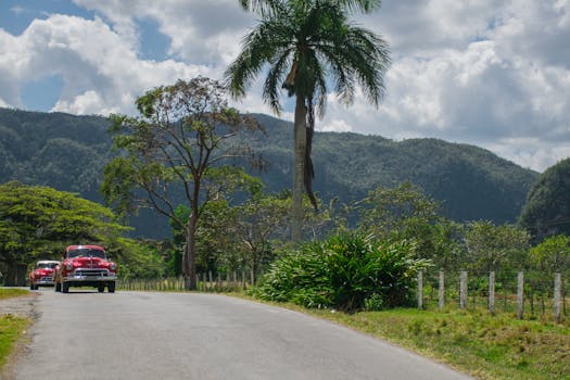 Vintage red cars on a scenic road in Vinales, Cuba surrounded by lush greenery and mountains.