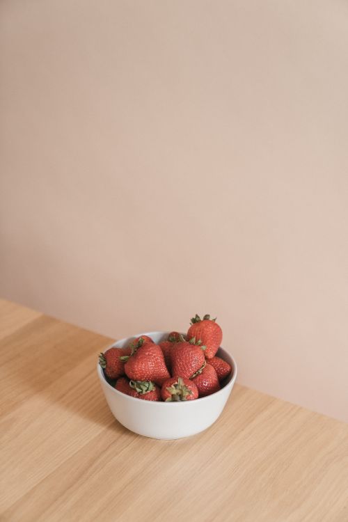 Free A bowl of fresh strawberries on a wooden table against a neutral wall, evoking simplicity and freshness. Stock Photo
