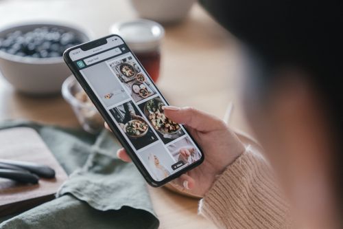 Free Close-up of a hand holding a smartphone browsing food recipes. Cozy kitchen setting. Stock Photo