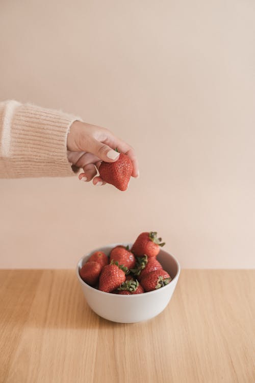 A Person Picking a Strawberry from a Bowl 