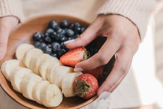 A wooden bowl filled with fresh bananas and berries held by an unrecognizable person's hands.