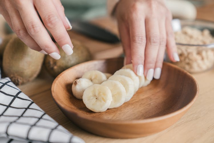 Person Arranging Sliced Banana On A Wooden Bowl