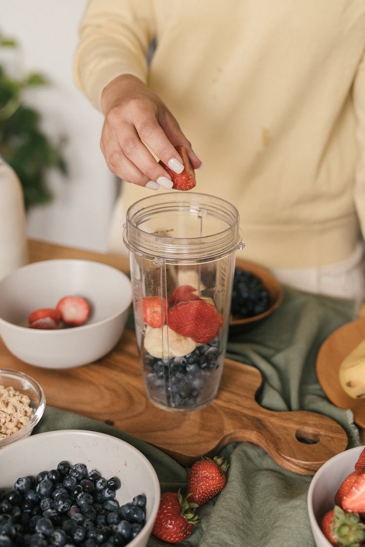 A Person Putting Fresh Fruit In A Blender Jar