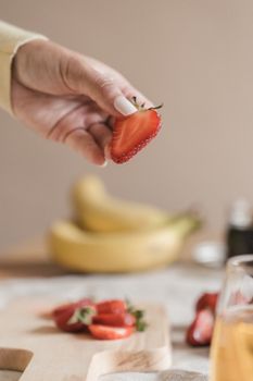 Close-up of a hand holding a fresh strawberry slice with bananas in the background.