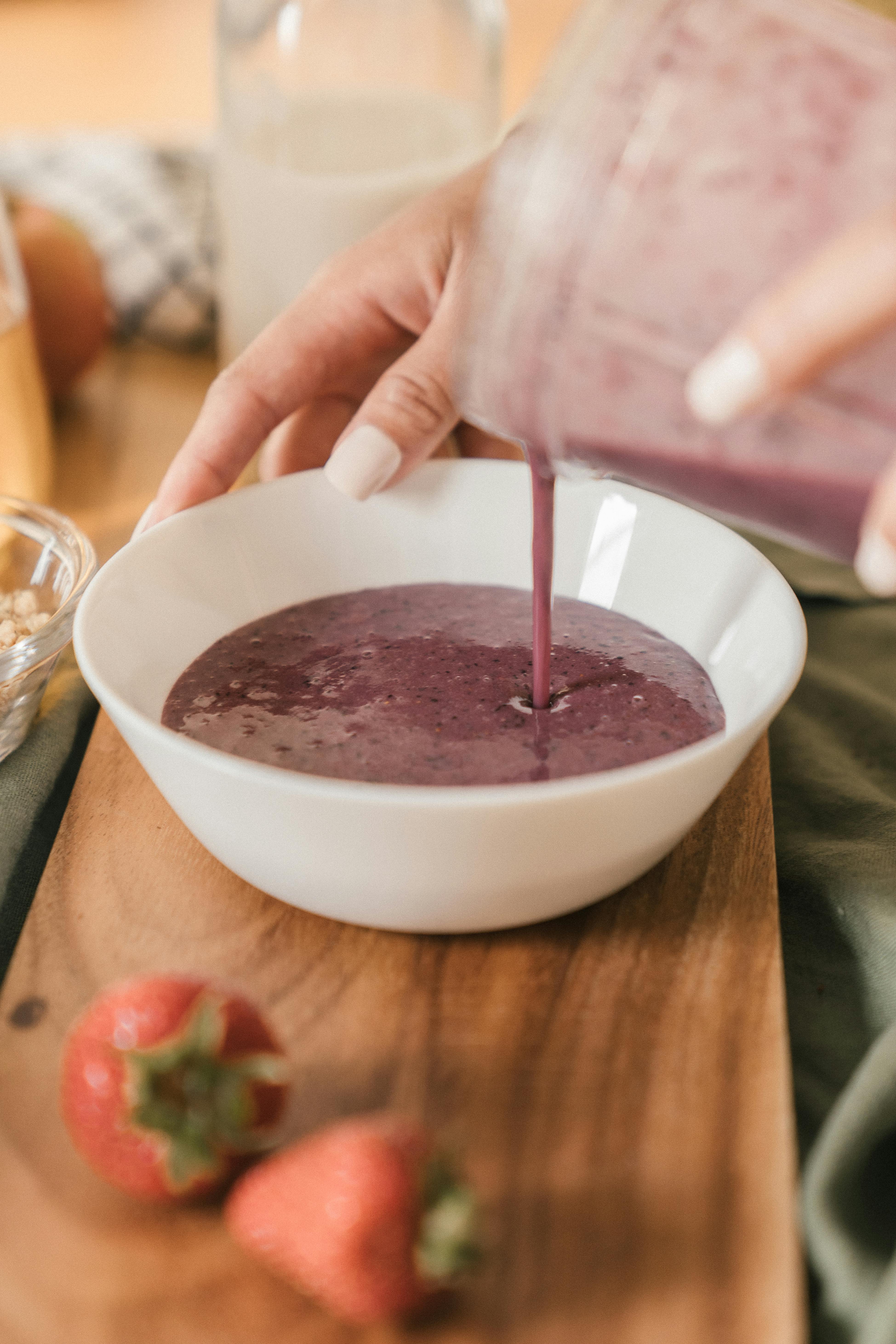 woman pouring purple juice in ceramic bowl