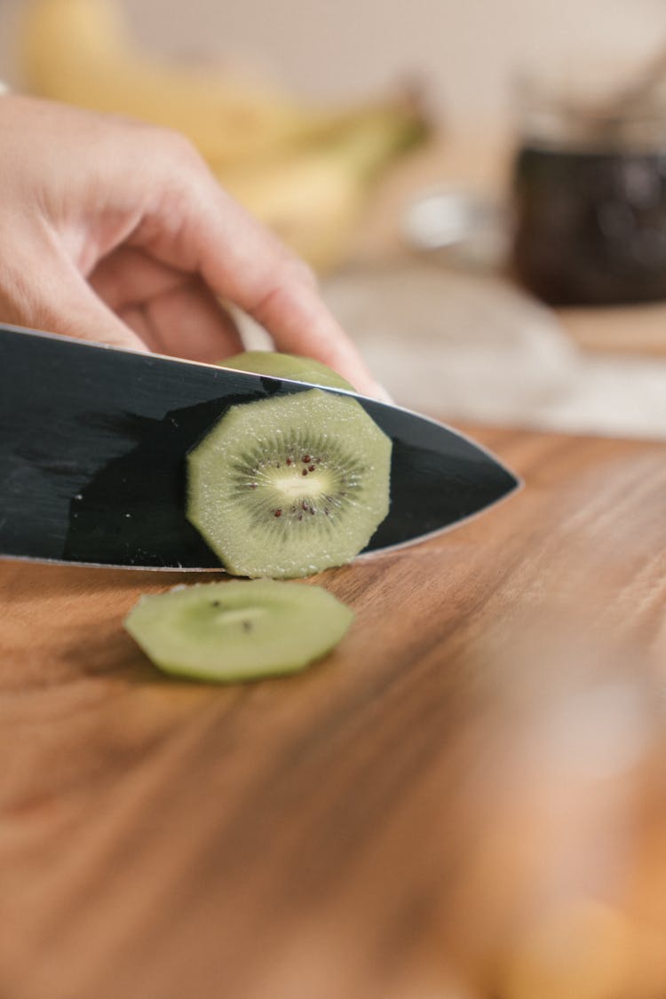 Close-up Of Person Cutting Kiwi With Knife