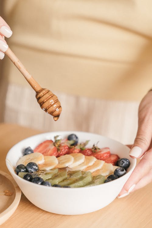 Person Holding White Ceramic Plate and a Wooden Spoon With Honey