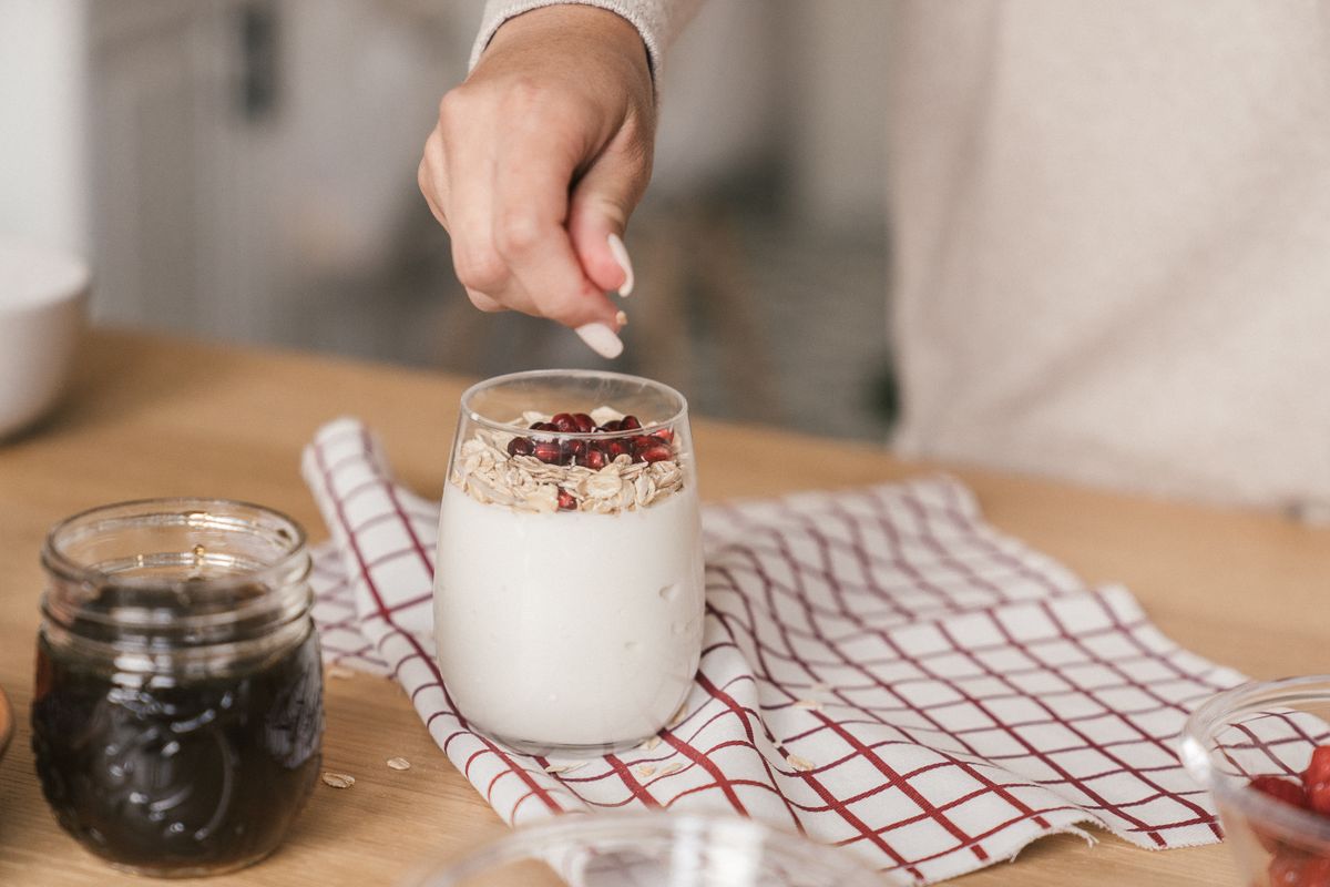 Person preparing yogurt with granola and pomegranate. A nutritious and delicious breakfast idea.