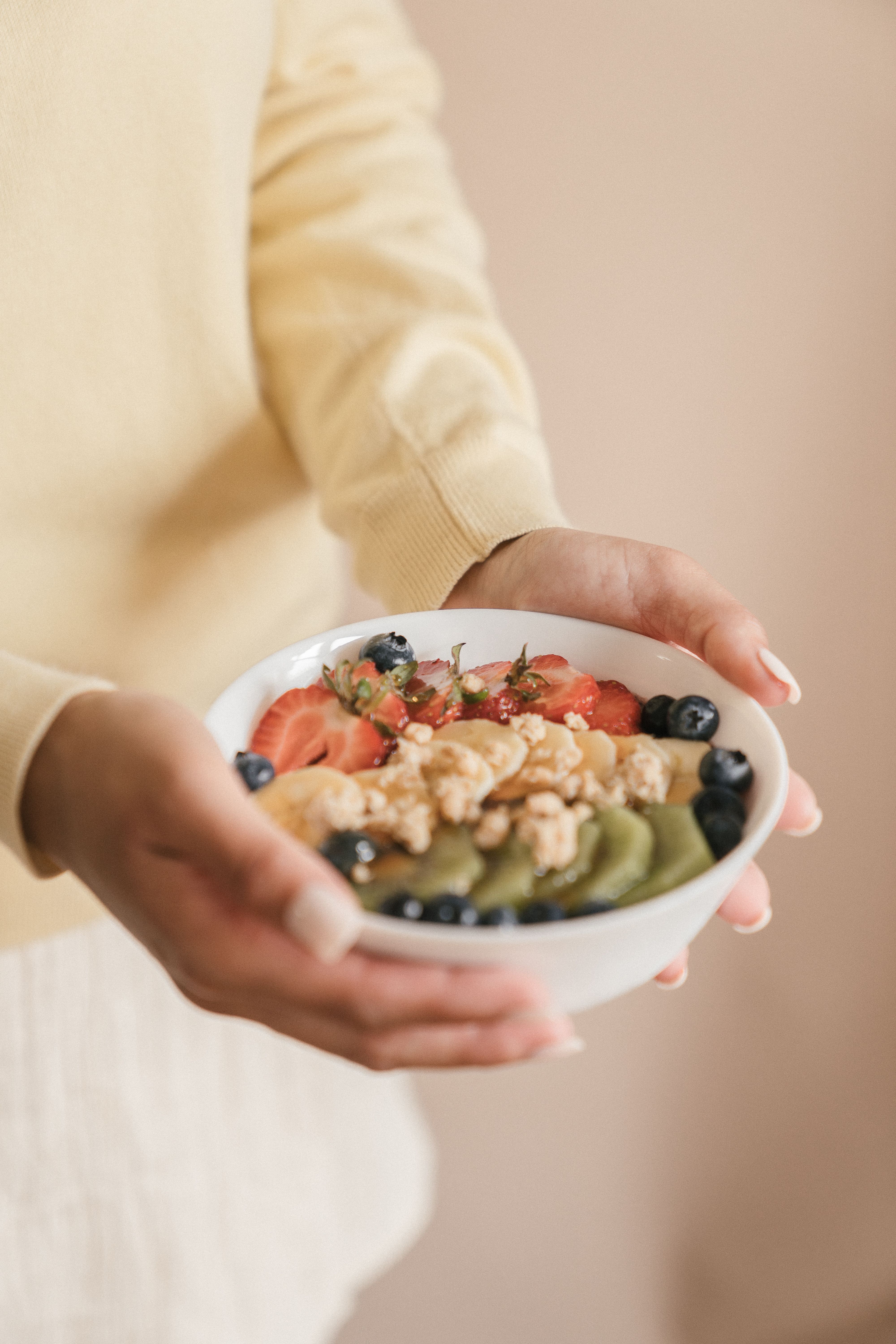 Mains tenant un bol de fruits et granola