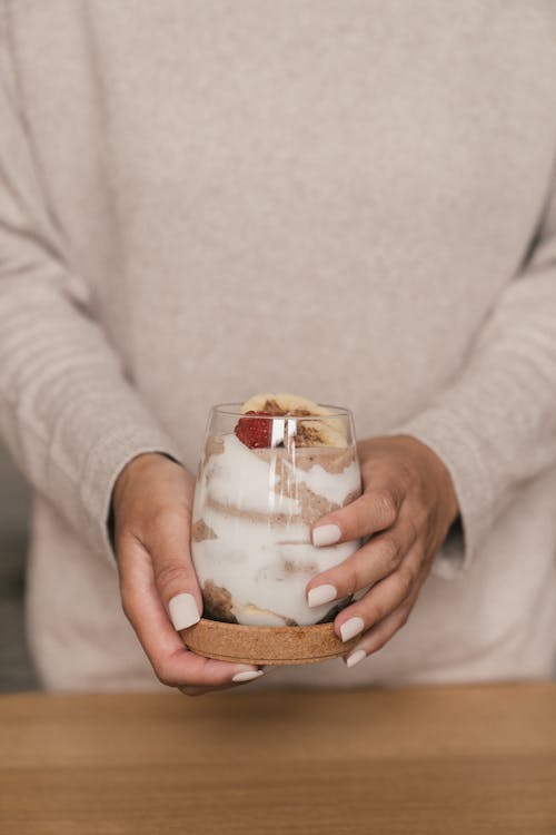 Free Person in Beige Long Sleeves Holding a Clear Glass of Yoghurt Stock Photo