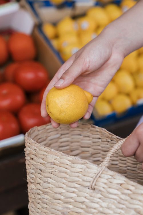 Free Close-up of a hand picking fresh lemons from a market display into a woven basket. Stock Photo