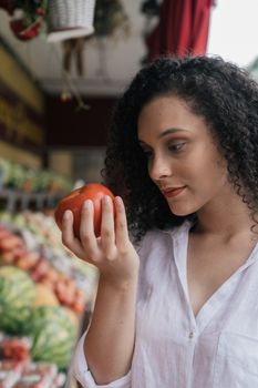 Woman in white shirt examining a tomato at an outdoor market.