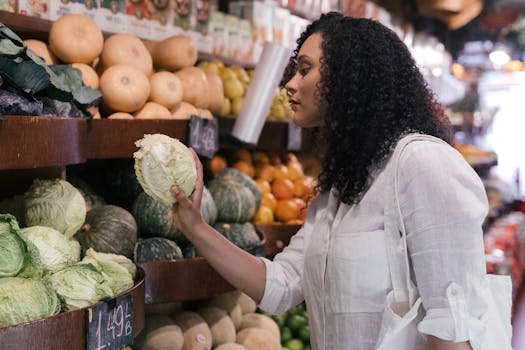 A woman in a white shirt selects fresh cabbage at an indoor market.
