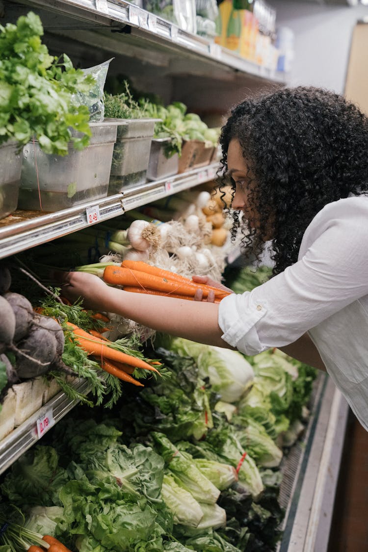 Woman In White Top Getting Carrots From The Vegetable Shelf