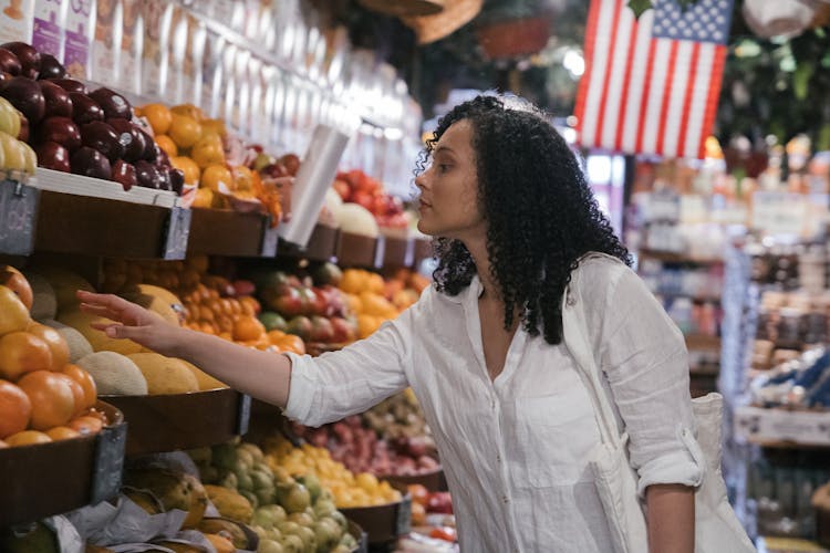 A Woman Looking For Vegetables And Fruits Inside The Market