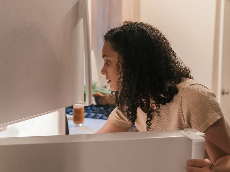 Woman checking the contents of an open refrigerator in a modern kitchen Woman checking the contents of an open refrigerator in a modern kitchen