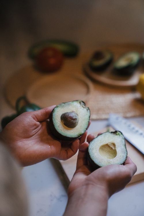 Free Close-up of hands holding ripe avocado halves in a cozy kitchen ambiance. Stock Photo