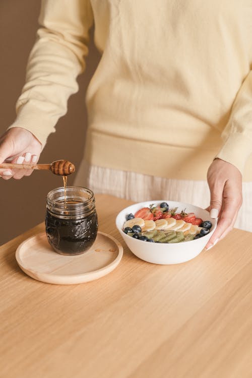 Woman Adding Honey to Fruit in a Bowl 