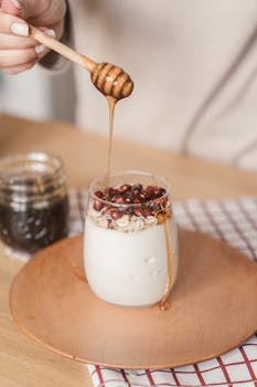 Close-up of honey drizzling onto yogurt topped with granola and pomegranate seeds.