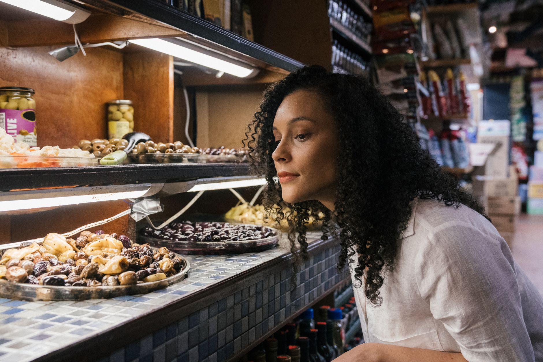 A woman examining a selection of olives in a gourmet food store with a variety of options.