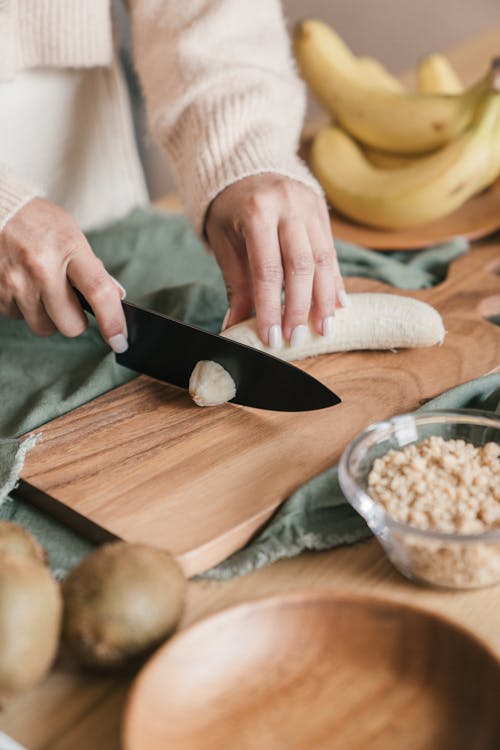 Person Slicing Banana on Wooden Chopping Board