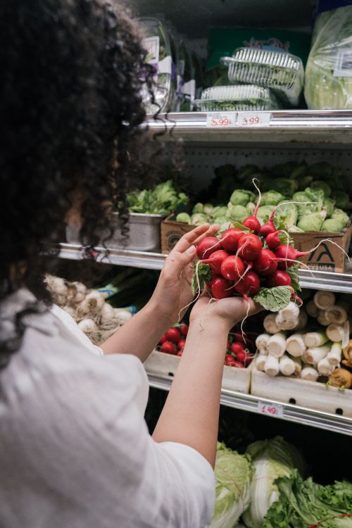 Free A shopper inspects radishes among fresh produce at a grocery market, seeking quality vegetables. Stock Photo