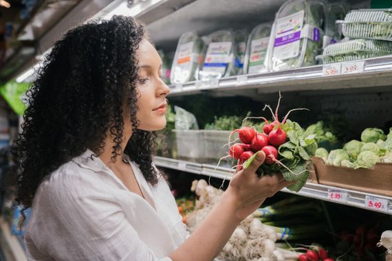 Mulher escolhendo rabanetes frescos em seção de vegetais no mercado