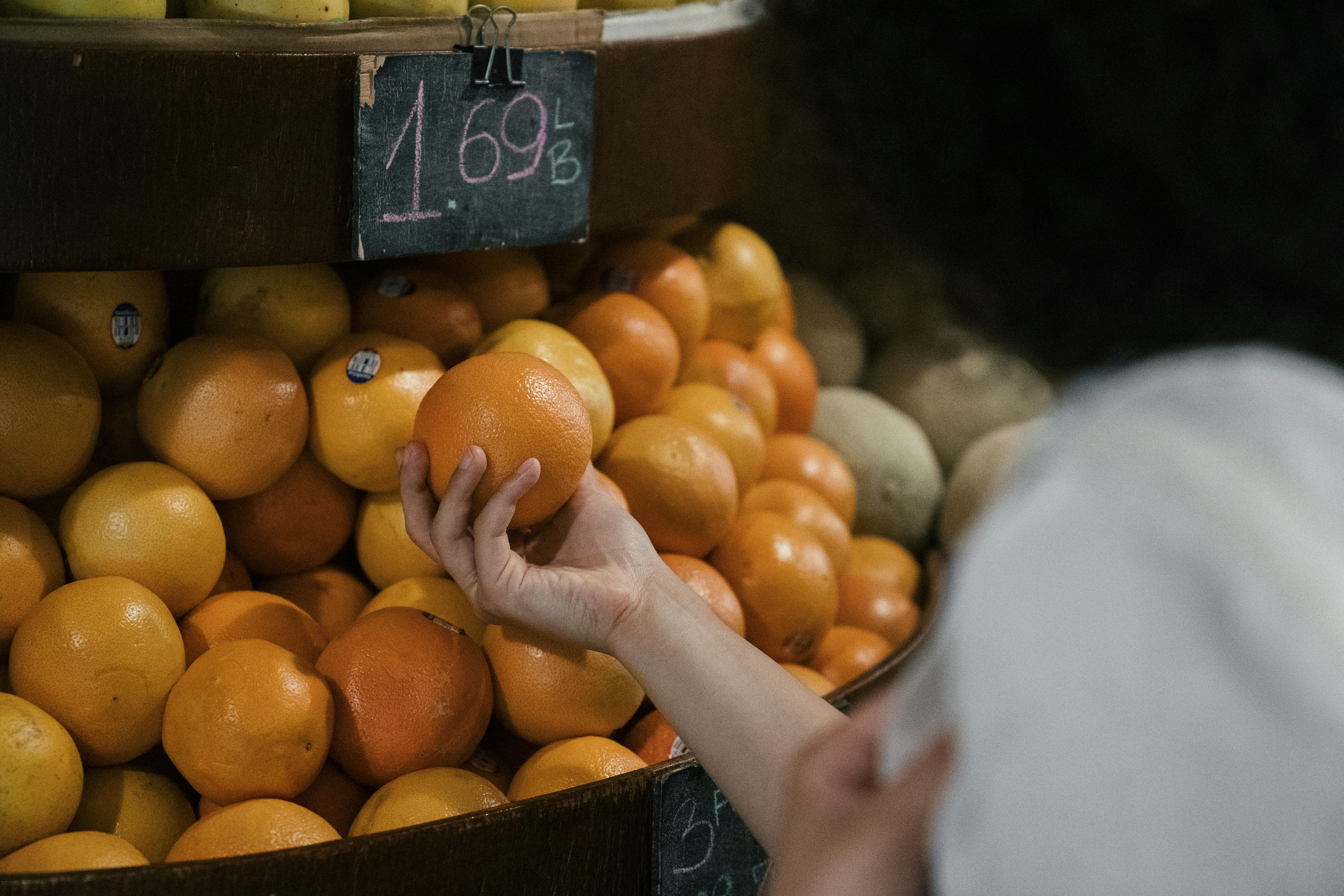 A person chooses oranges from a market display, showcasing freshness and healthy choices.