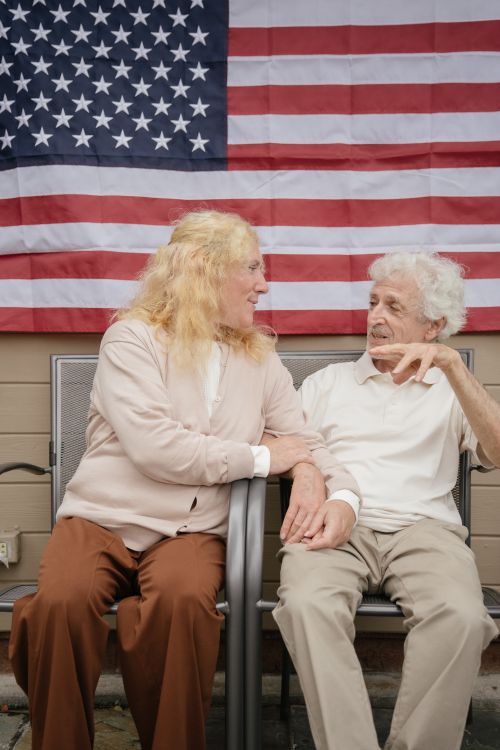 Free An elderly couple conversing in front of an American flag, showcasing intimacy and patriotism. Stock Photo