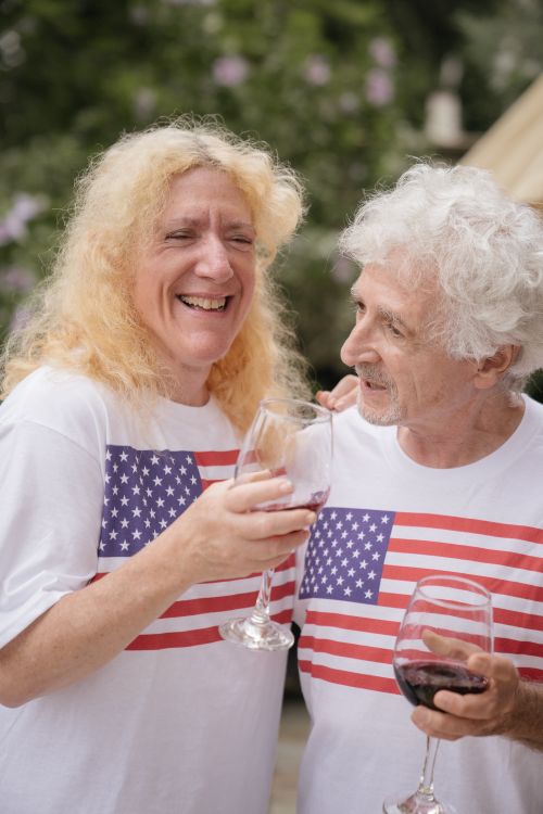 Free Happy senior couple in American flag shirts enjoying wine outdoors. Stock Photo