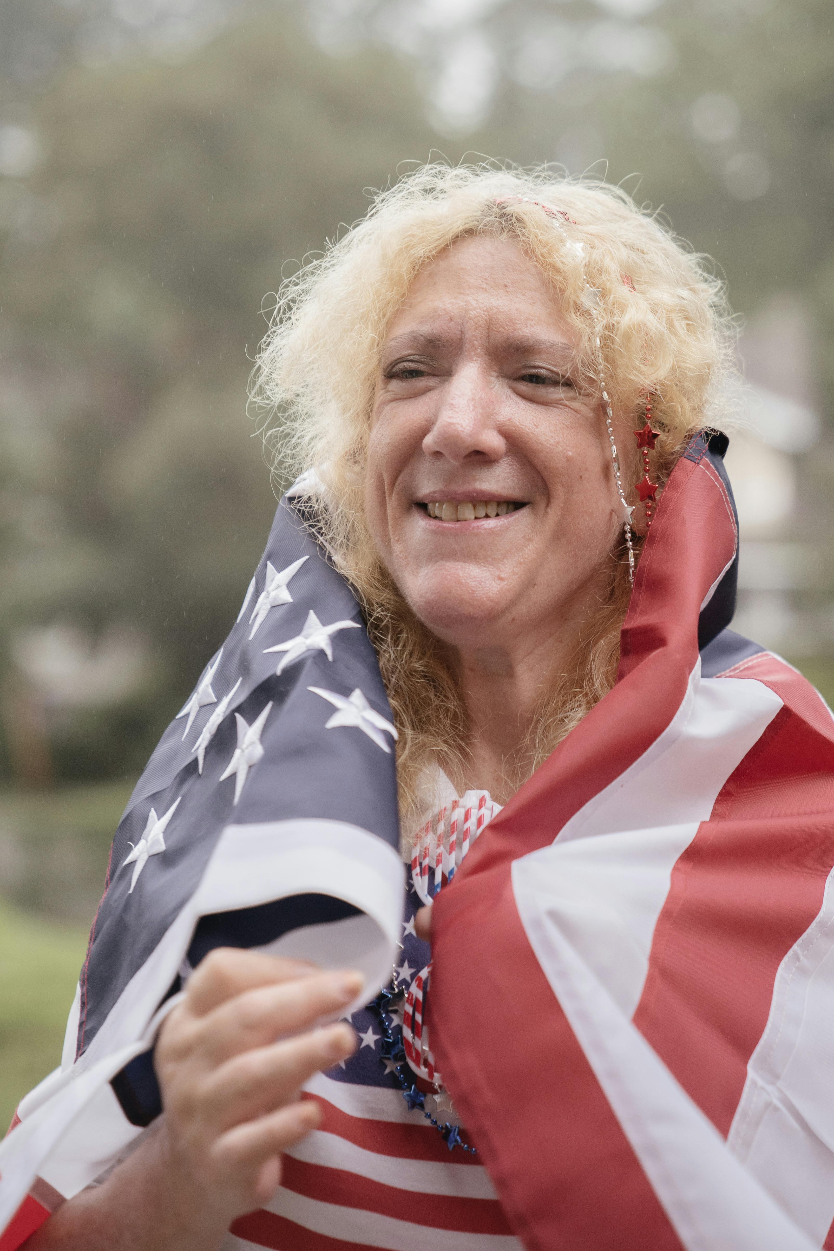 Senior adult celebrating patriotism wrapped in American flag outdoors.