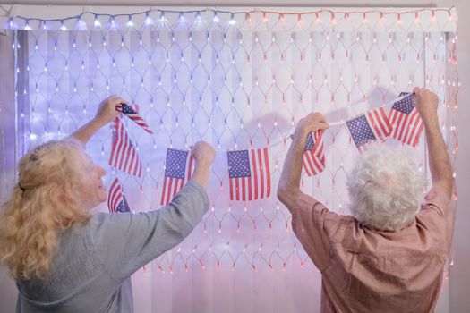 Elderly couple hangs American flags indoors for a patriotic celebration.