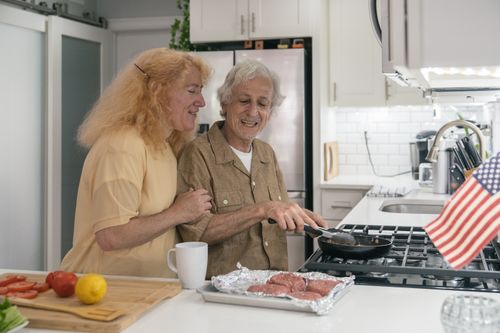 Free A senior couple enjoys cooking burgers in their modern kitchen, celebrating with joy. Stock Photo