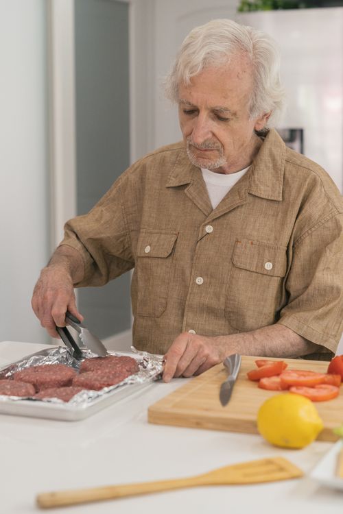 Free Elderly man cooking burgers in a home kitchen, showcasing food preparation. Stock Photo
