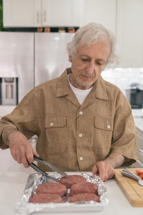 Free An elderly man preparing raw hamburger patties in a home kitchen setting. Stock Photo
