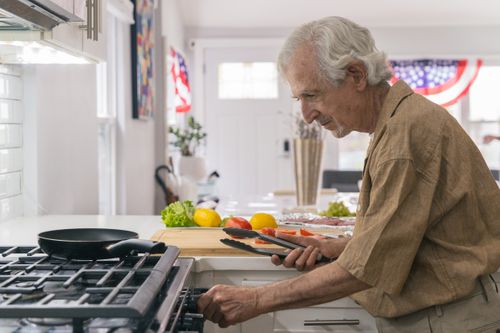 Free Elderly man enjoying home cooking preparation in a bright, modern kitchen. Stock Photo