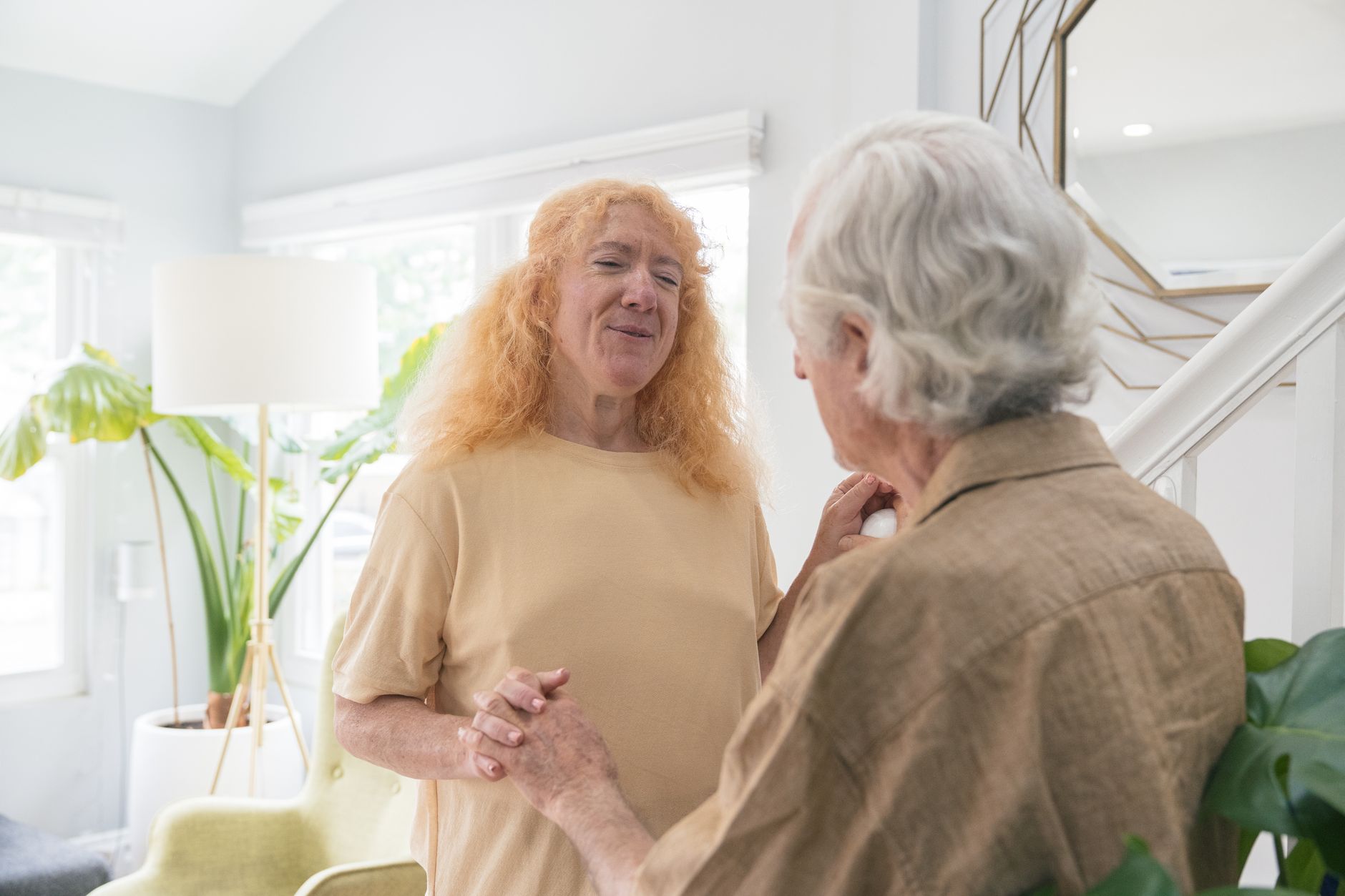 An elderly couple sharing a warm and tender moment indoors, holding hands and smiling at each other.