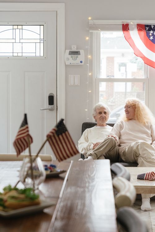 Free An elderly couple sitting together indoors with American flags, enjoying a cozy 4th of July celebration. Stock Photo