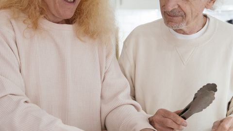 Elderly couple enjoying time in the kitchen preparing sandwiches together, showcasing warmth and togetherness.