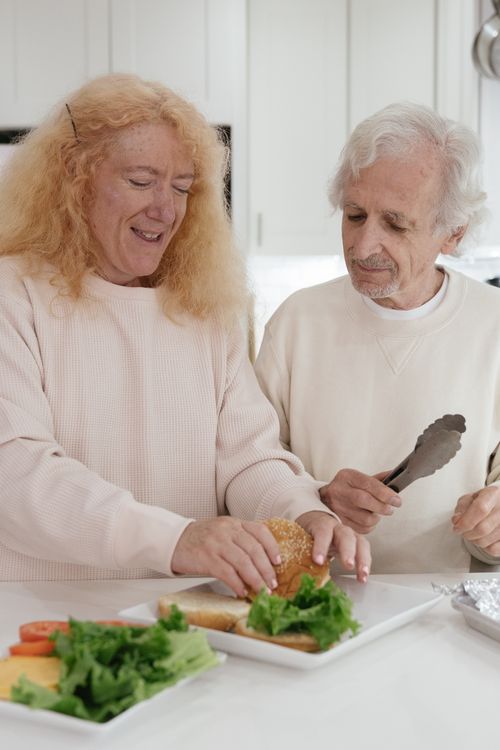 Free Elderly couple enjoying time in the kitchen preparing sandwiches together, showcasing warmth and togetherness. Stock Photo